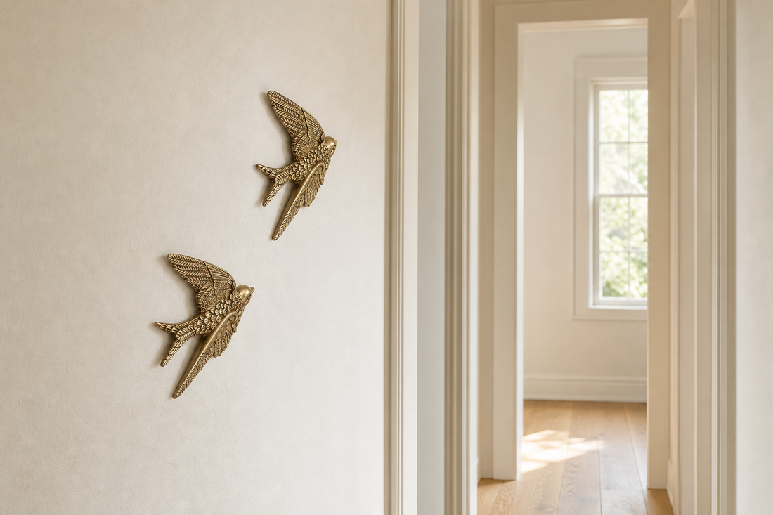 Two small gold-tone swallow wall sculptures arranged diagonally on a narrow light hallway wall