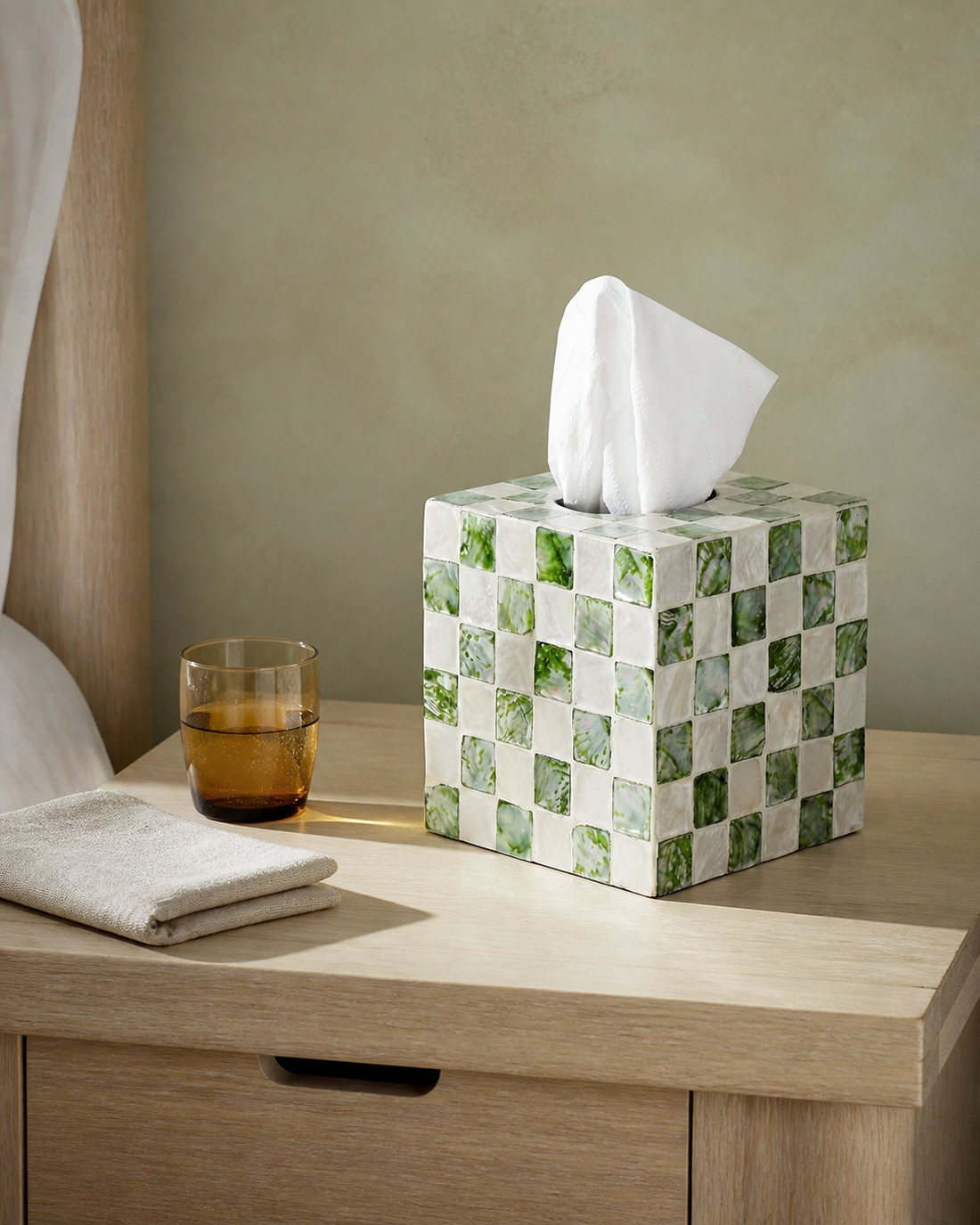 Green and white capiz tissue box cover on a pale oak bedside table with open pull space above it